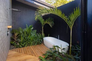 A modern bathroom with a freestanding bathtub, surrounded by lush greenery and a wooden deck. - Villa la Selva (Reserva de Golf, Hacienda Pinilla)