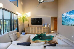 A modern living room with a large sofa, a coffee table, a television, and a painting on the wall. - Villa la Selva (Reserva de Golf, Hacienda Pinilla)