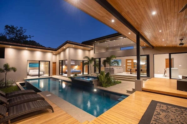 A modern house with a swimming pool, outdoor seating, and a well-lit interior.