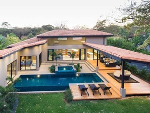 Una casa moderna de dos pisos con piscina, mobiliario exterior y un patio.