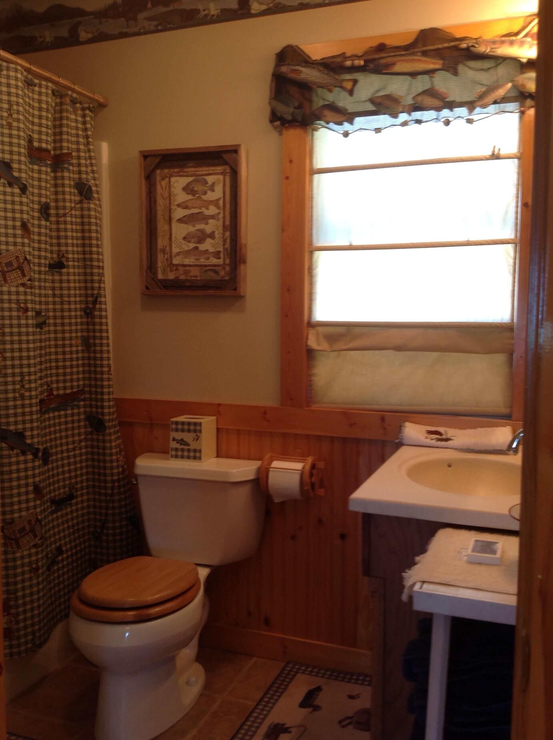 Un baño con inodoro de madera, un mural enmarcado de peces, una ventana con cortina y un lavabo con toalla.