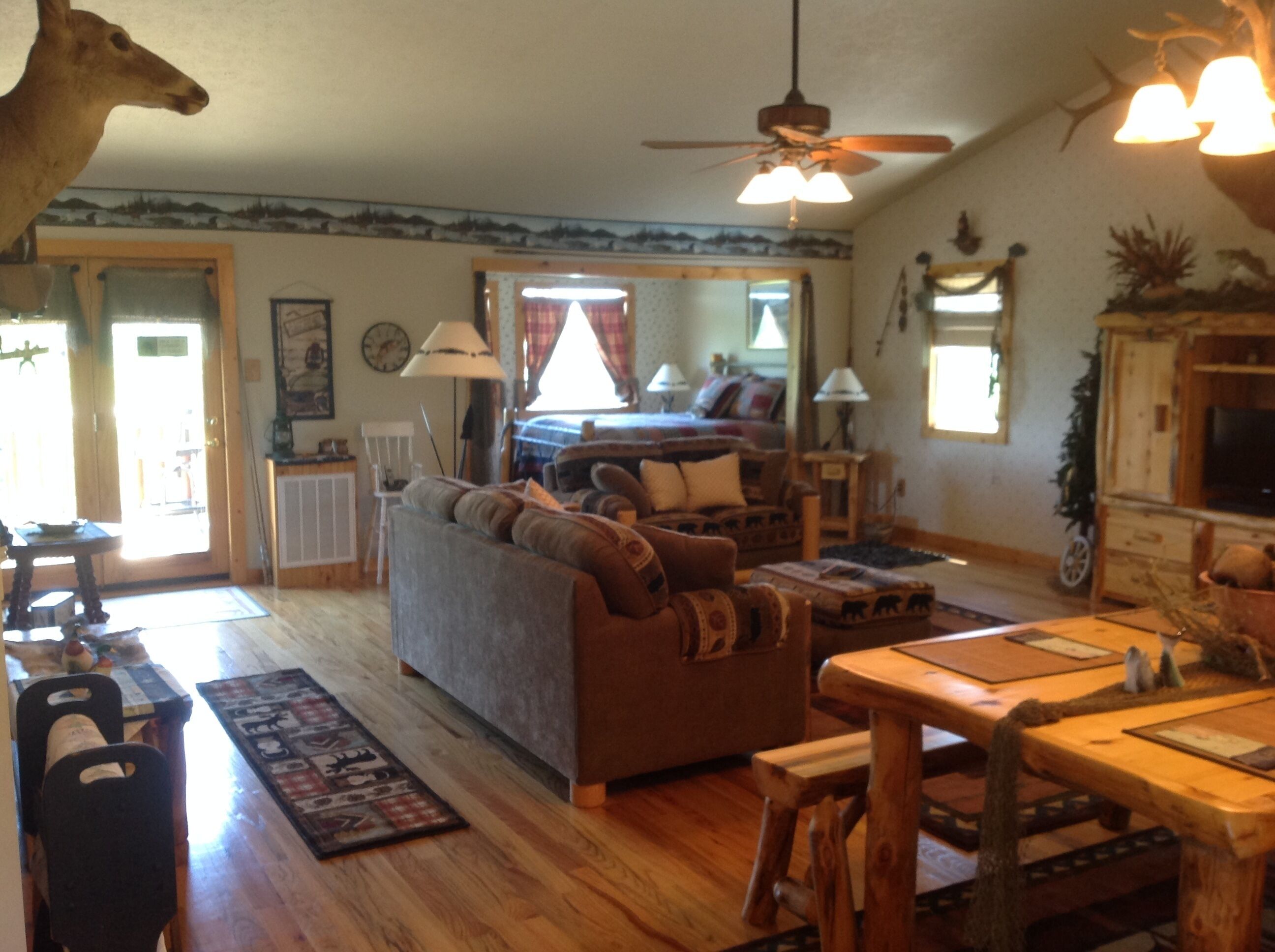 A cozy living room with a sofa, wooden coffee table, and a ceiling fan. A dining area with a wooden table and chairs is visible.