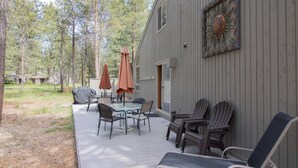 An outdoor patio with a table and chairs, surrounded by Adirondack chairs, and a covered seating area with umbrellas.