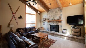 A cozy living room with a stone fireplace, leather sofa, and a flat-screen TV.