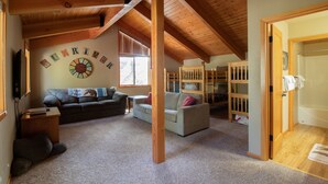 A cozy loft-style living room with exposed wooden beams, a large window, and a loft bed.