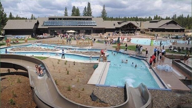 A water park with multiple pools, a large slide, and a building with solar panels in the background.