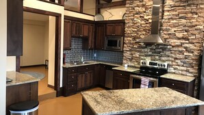 A modern kitchen with dark wood cabinets, granite countertops, a stone backsplash, and stainless steel appliances.