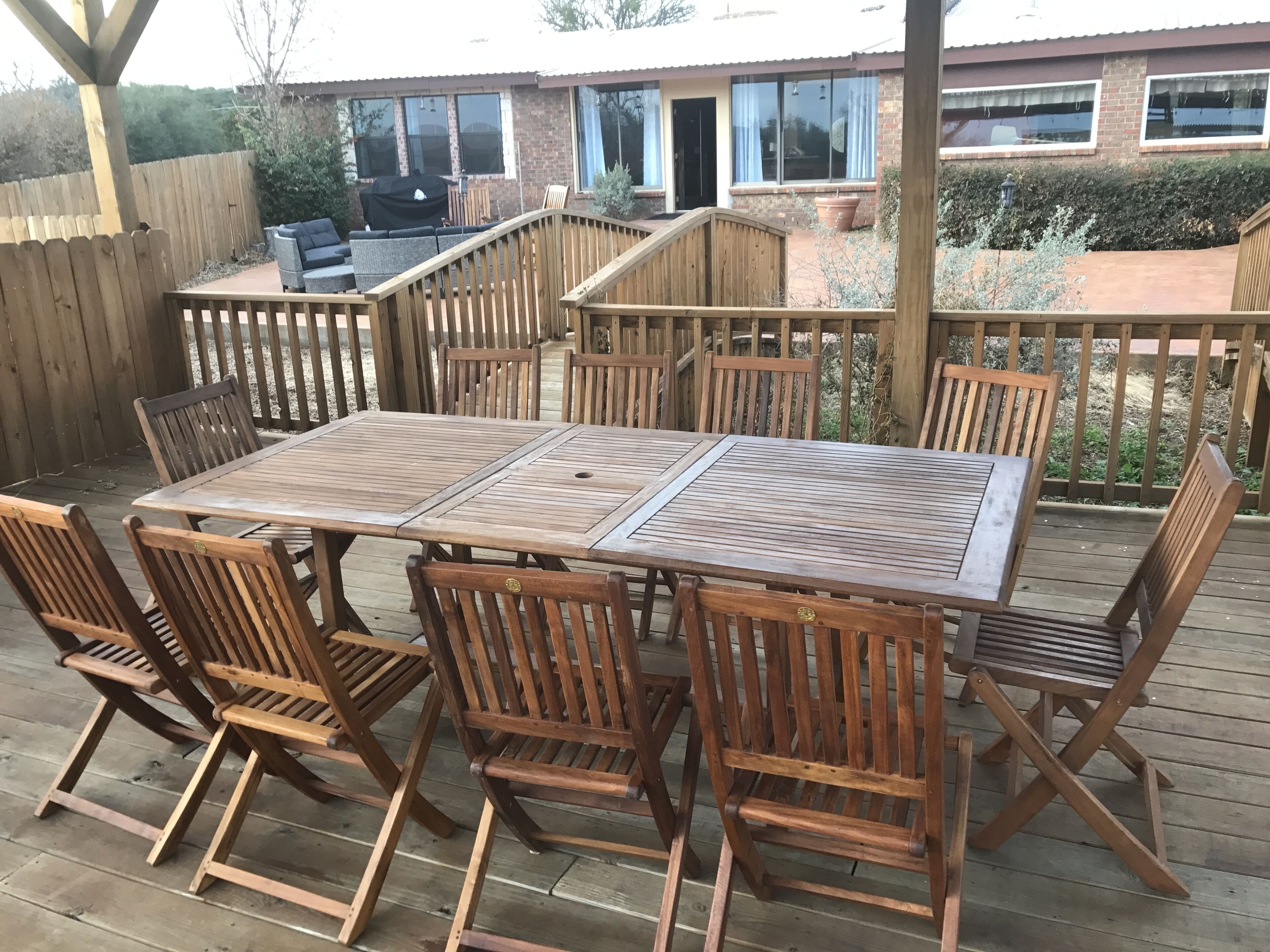 Eine Holzterrasse mit Tisch und Stühlen, einem Grill und einem Haus im Hintergrund.