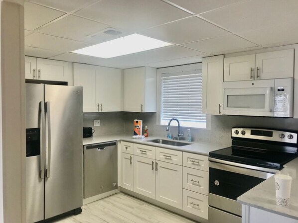 A modern kitchen with stainless steel appliances, white cabinetry, and a window with blinds.