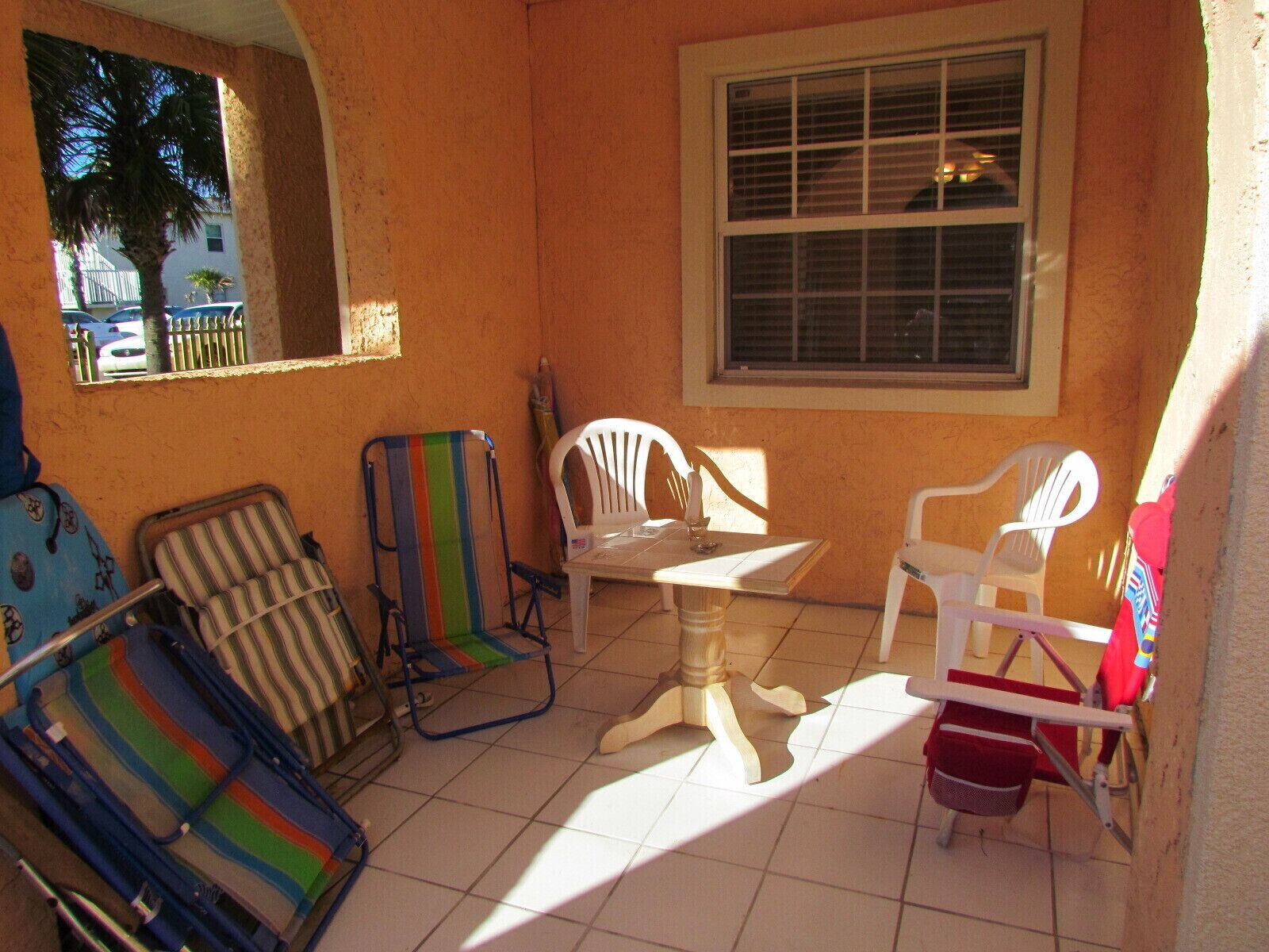 A sunlit patio with a table and four chairs, a striped beach chair, and a red bucket.