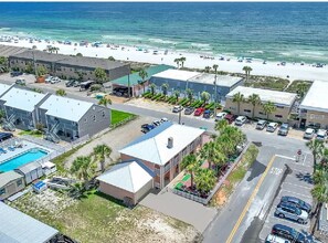 An aerial view of a coastal hotel with a swimming pool, parking lot, and beach access.