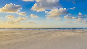 A beach with a wide sandy shore and a clear sky with scattered clouds.