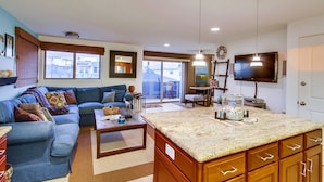 A modern living room with a blue sofa, a coffee table, and a kitchen area with a granite countertop.