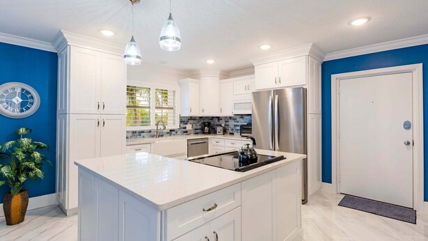 Una cocina moderna con armarios blancos, una isla central, electrodomésticos de acero inoxidable e iluminación colgante.