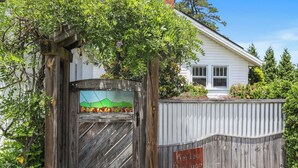Una reja de madera con un panel de vidrio que muestra el paisaje, un cartel de metal que dice "Perley Produce" y una casa blanca con techo rojo al fondo.