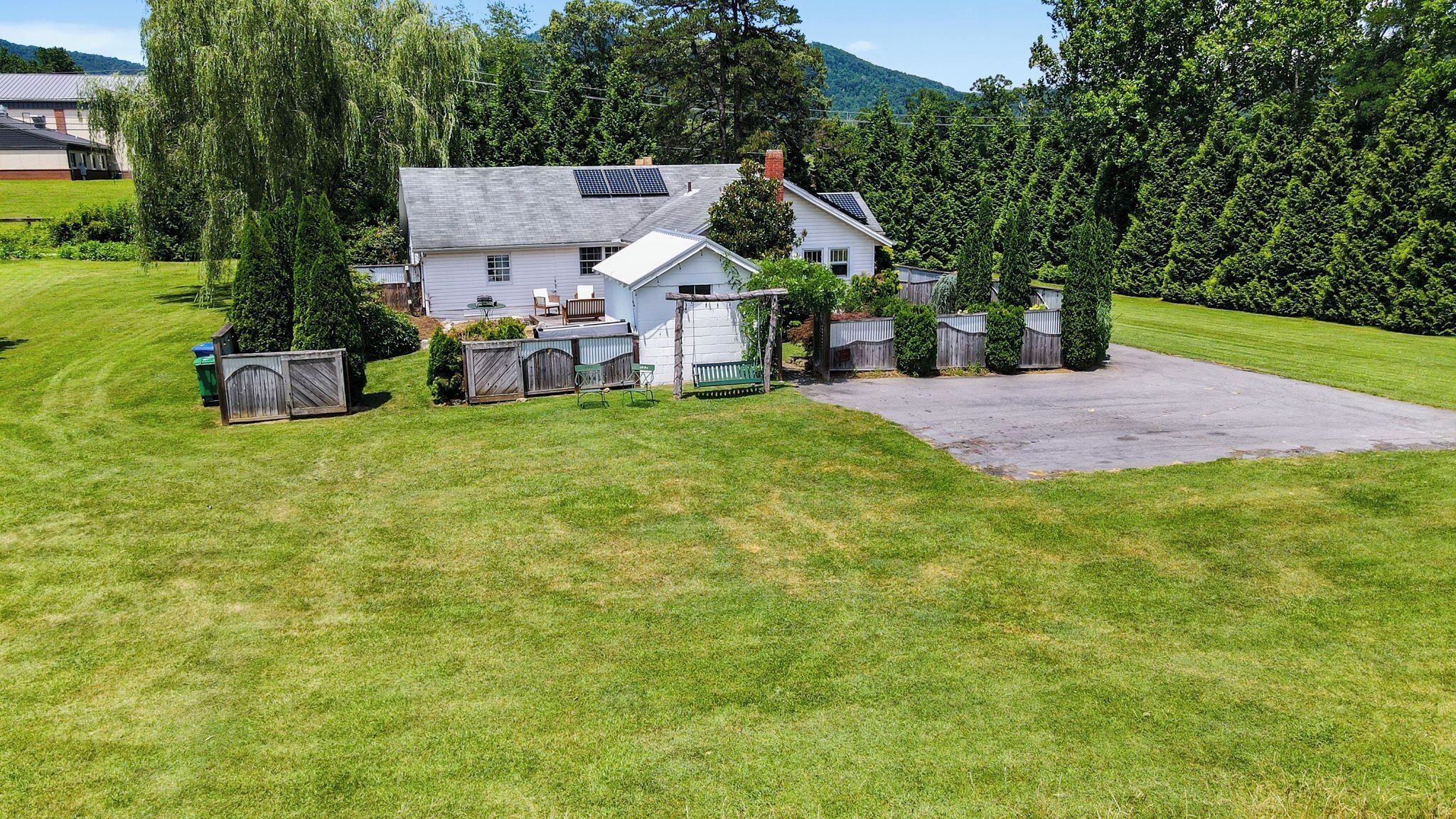 Une maison de plain-pied avec un toit en pente, des panneaux solaires et une cour clôturée.