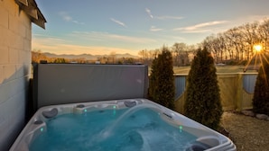 Jacuzzi con vistas a montañas y árboles al atardecer.