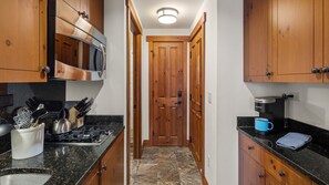 Una cocina estrecha con armarios de madera, un refrigerador de acero inoxidable, una cafetera y una estufa.