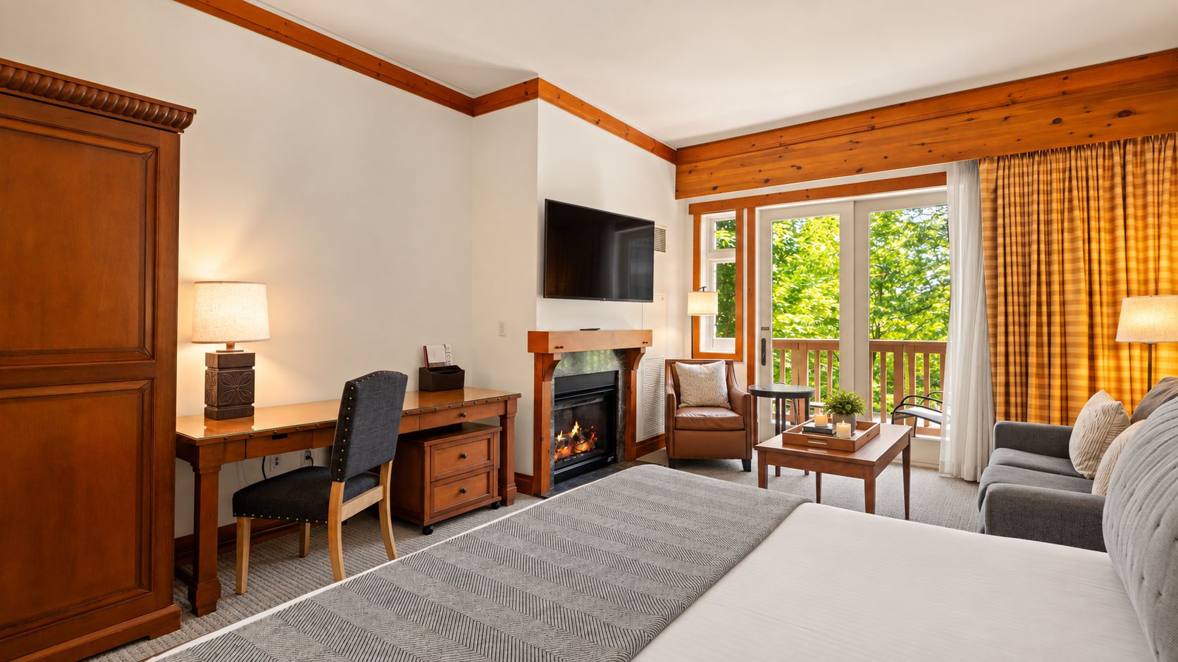Ein Hotelzimmer mit Bett, Schreibtisch mit Stuhl, Fernseher, Kamin und einer Couch.