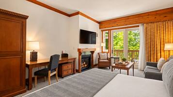 A hotel room with a bed, a desk with a chair, a television, a fireplace, and a sofa.