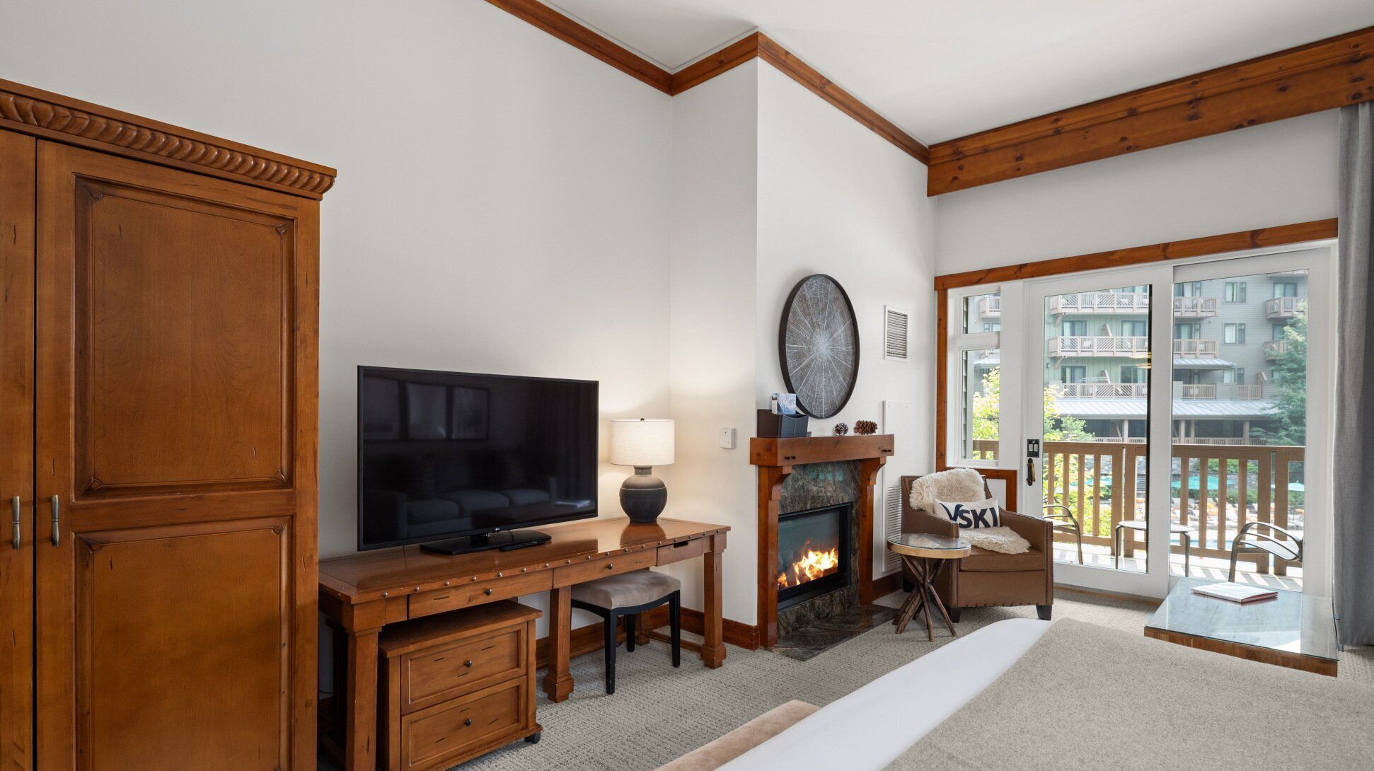 A hotel room with a wooden desk, television, fireplace, and a view of the outside balcony.