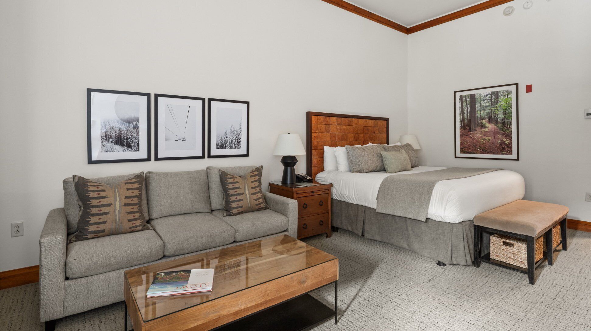 A modern hotel room with a sofa, a bed, a nightstand, and a coffee table. There are three framed pictures on the wall.