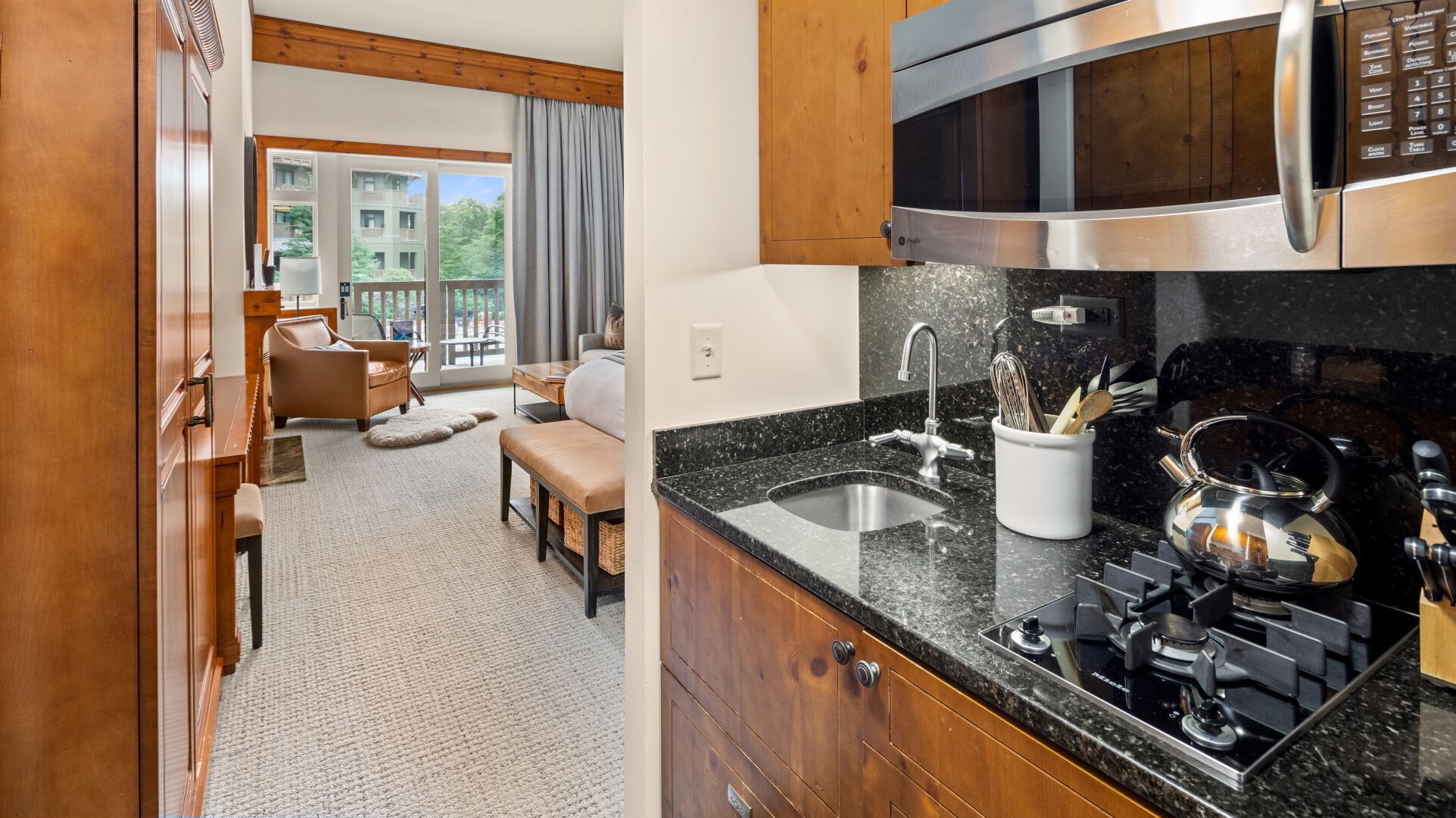 A modern kitchen with a built-in oven, microwave, and stove. There is a wooden dining area with a bench and a view of the outside.