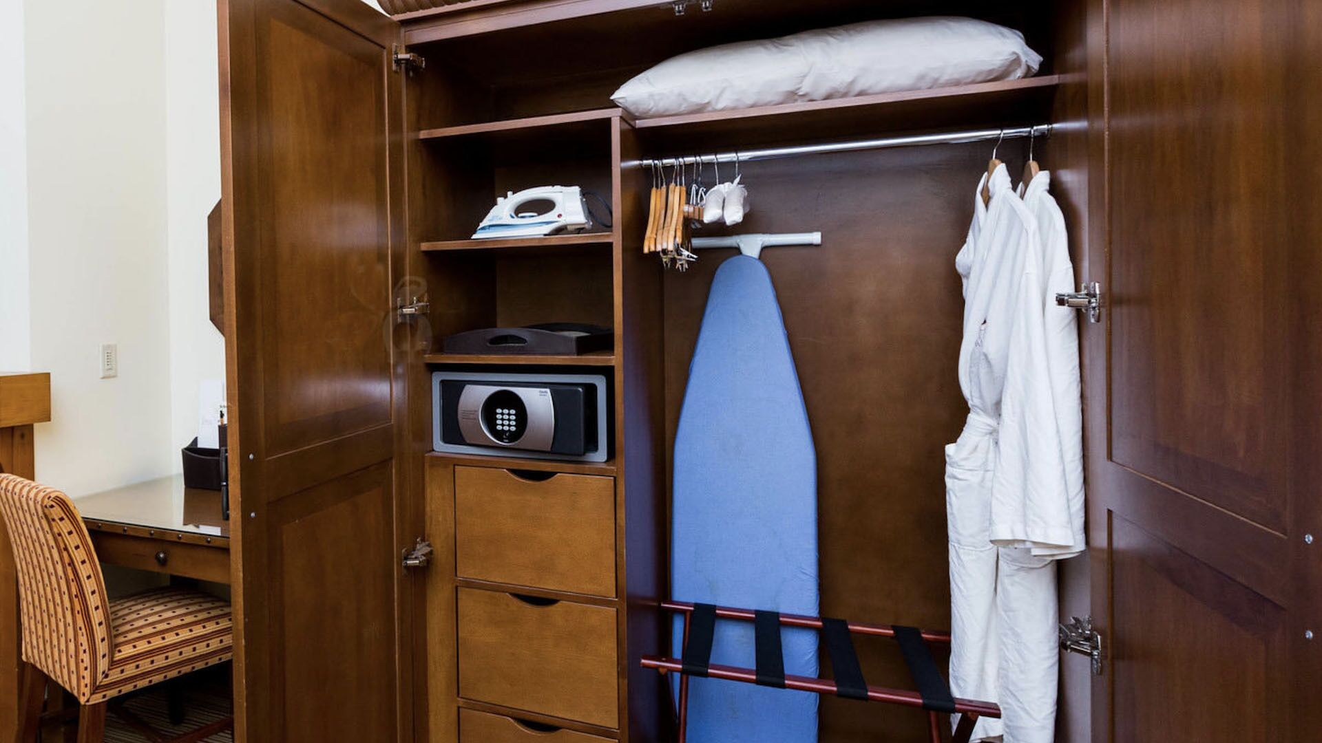 A compact room with a wooden wardrobe, a small ironing board, and a blue ironing board.