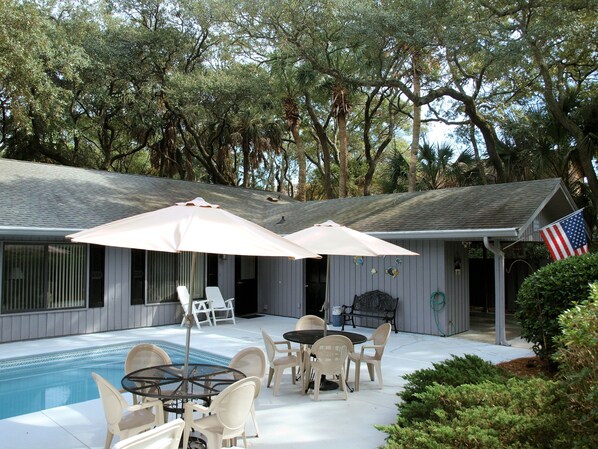 A poolside area with a table and chairs, an American flag, and a covered patio with umbrellas.