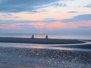 A beach with two cyclists and a sunset in the background.