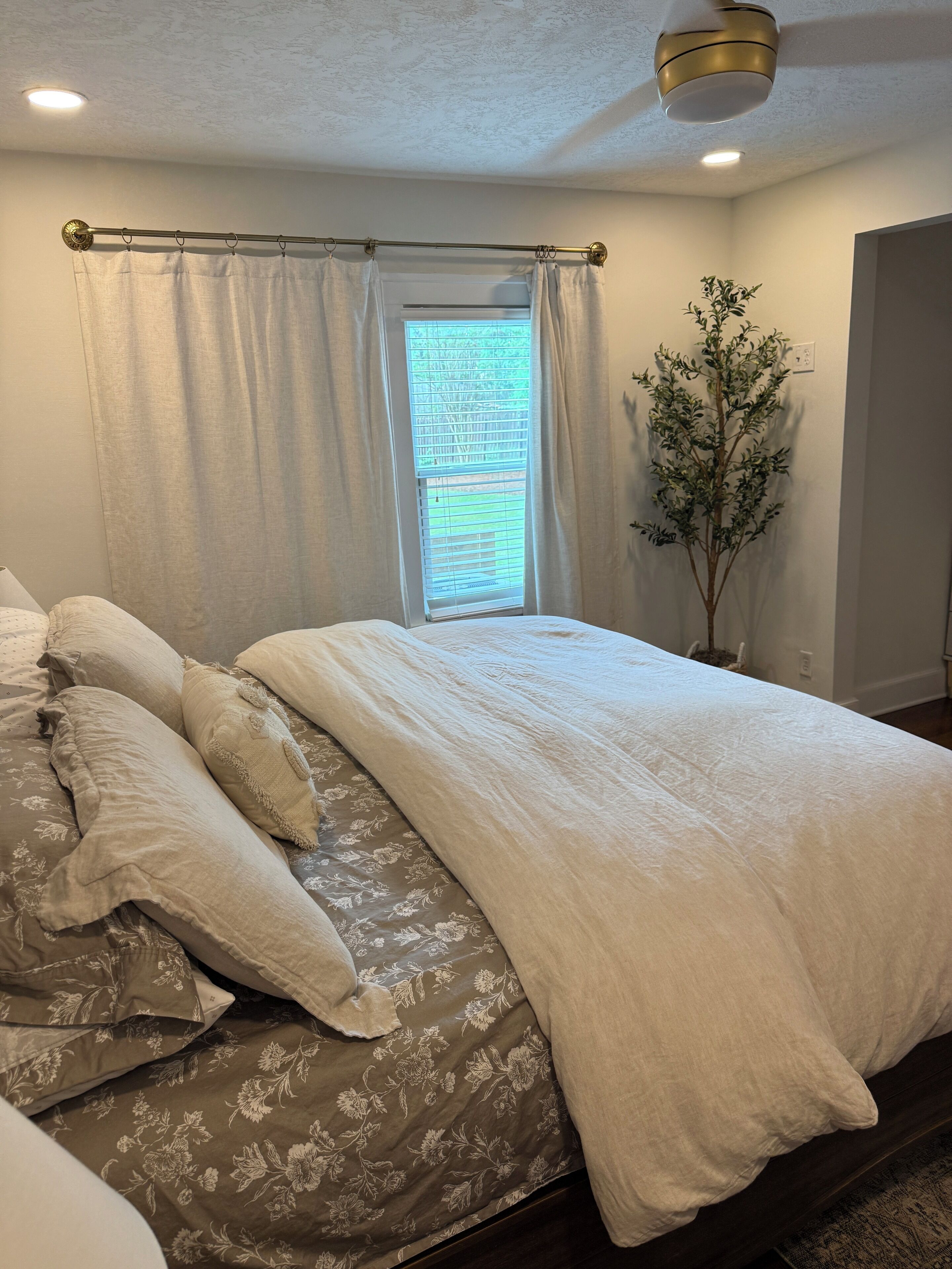Un dormitorio con cama, cortinas, una ventana y una planta.