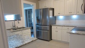 A kitchen with white cabinets, a stainless steel refrigerator, granite countertops, and a tiled floor. - Beautiful home near the Augusta National (Augusta)