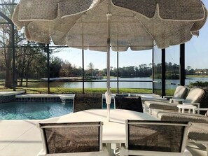 A poolside area with a table and chairs, a large umbrella, and a view of a lake and golf course. - Lakeside house, huge south facing pool with spa,  lake view, Disney at 8 miles (Kissimmee)