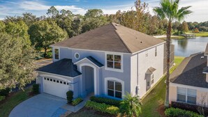 A two-story house with a garage, surrounded by a well-maintained lawn and a lake view. - Lakeside house, huge south facing pool with spa,  lake view, Disney at 8 miles (Kissimmee)