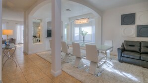 A spacious living room with a modern chandelier, a dining area with a glass table and chairs, and a black leather sofa. - Lakeside house, huge south facing pool with spa,  lake view, Disney at 8 miles (Kissimmee)