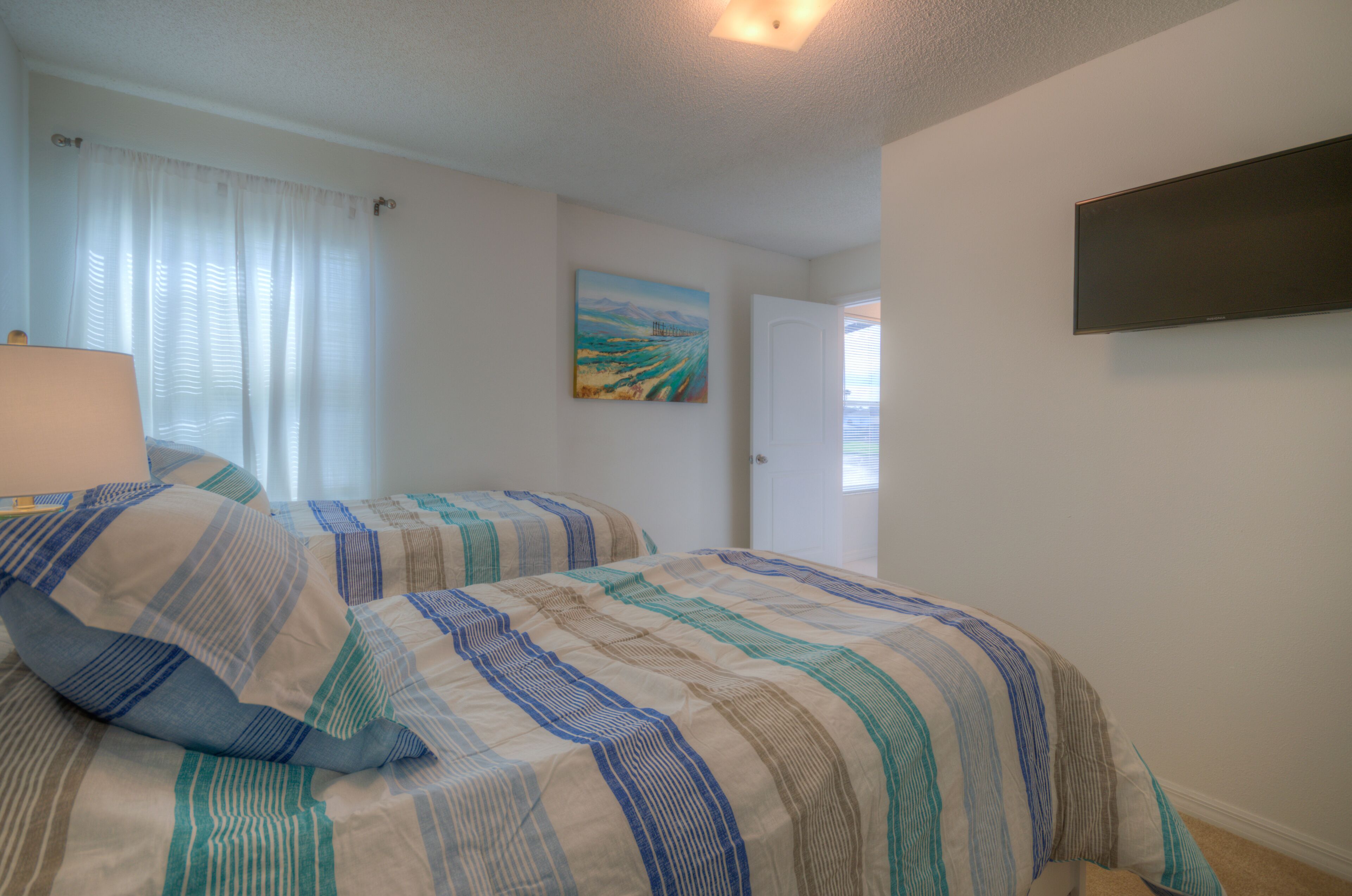 Ein Schlafzimmer mit zwei Betten, einem Bild an der Wand und einem an der Wand befestigten Fernseher.
