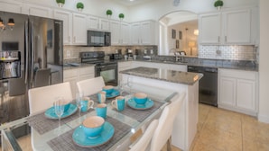 A modern kitchen with white cabinets, stainless steel appliances, and a dining area with blue tableware. - Lakeside house, huge south facing pool with spa,  lake view, Disney at 8 miles (Kissimmee)