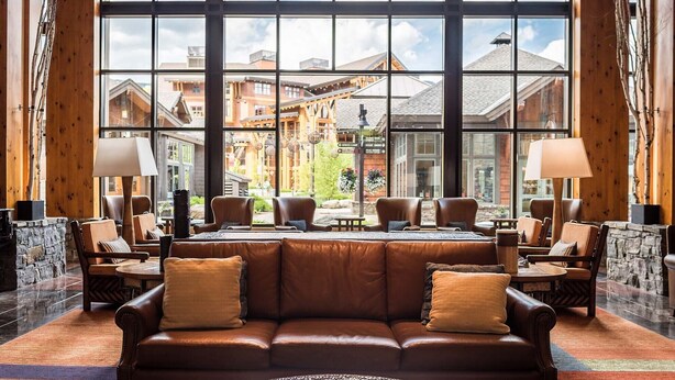 Eine Lobby mit einer Ledersofa, mehreren Sesseln, einem Couchtisch und einem großen Fenster mit Blick auf Gebäude und eine Steinmauer.