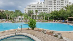 Una piscina con sillones de descanso y palmeras, rodeada por un edificio de hotel.