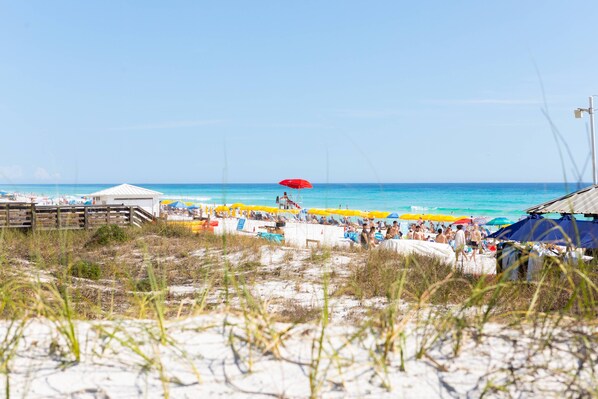 A beach with a wooden boardwalk, beach umbrellas, and a clear blue sky.