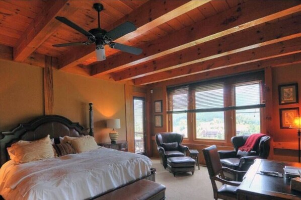 Une chambre avec un grand lit, un ventilateur de plafond et une vue sur l’extérieur par les fenêtres.