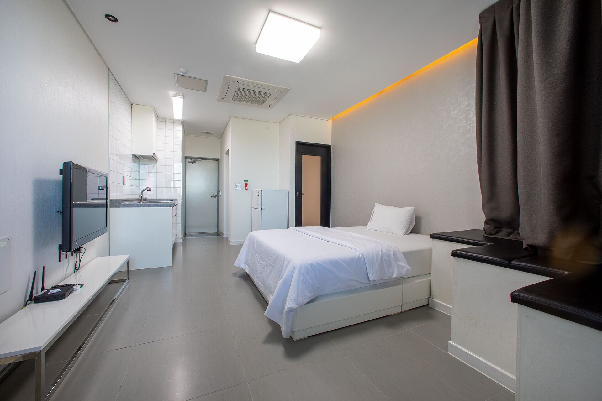 A hotel room with a bed, a desk, a flat-screen TV, a kitchenette, and a bathroom.