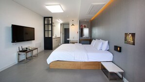 Habitación de hotel moderna con una cama grande, televisor, escritorio y baño visible a través de una puerta abierta.
