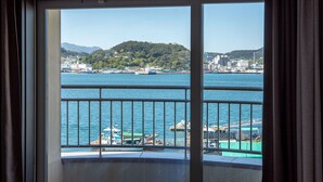 Vista desde un balcón con barandilla, sobre un cuerpo de agua con barcos y un horizonte urbano distante.