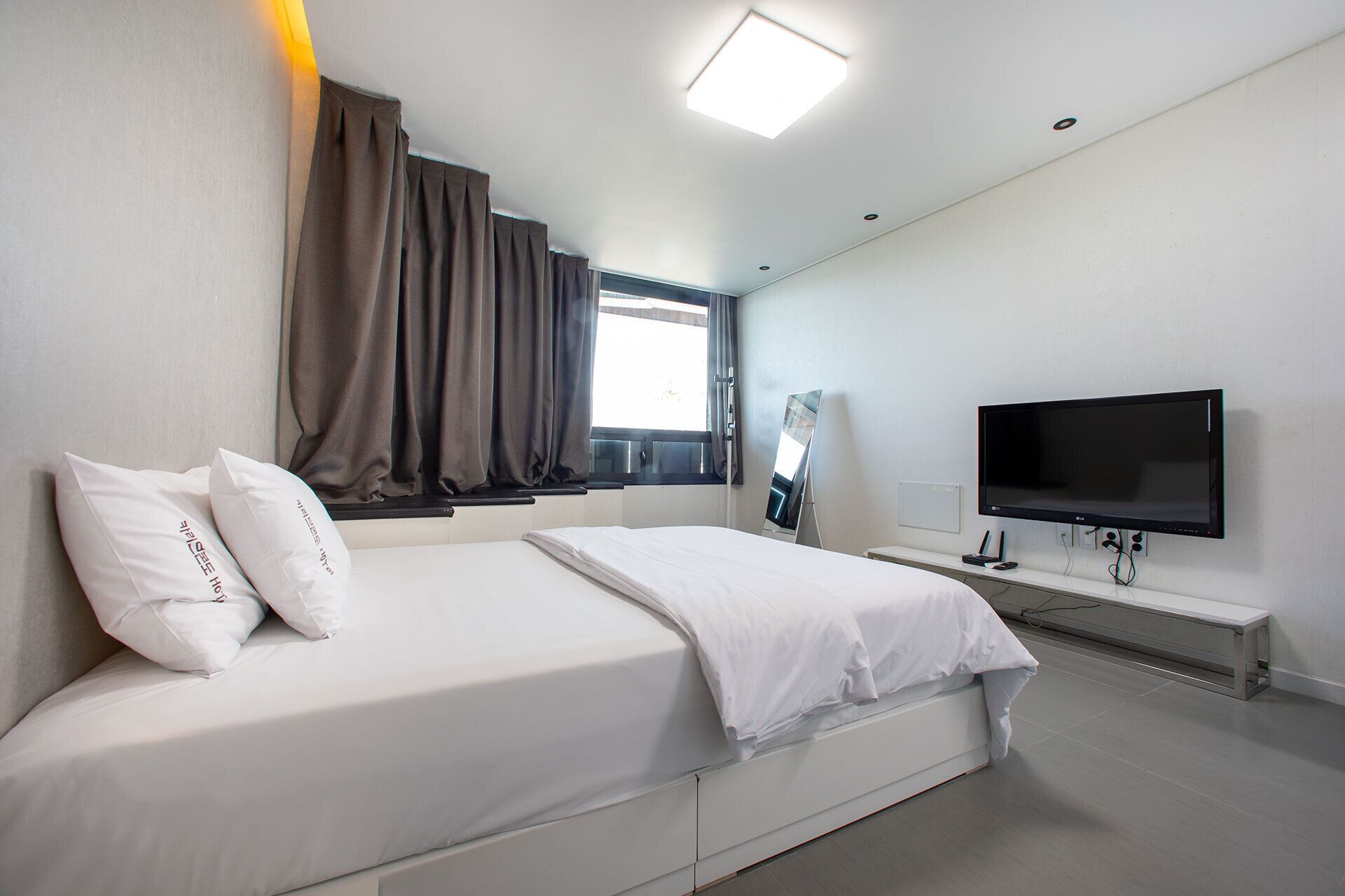 A modern hotel room with a large bed, a flat-screen TV, and a window with curtains.