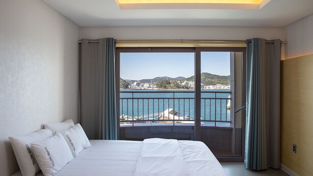 Habitación de hotel con una cama grande, vistas al mar y un balcón con barandilla.