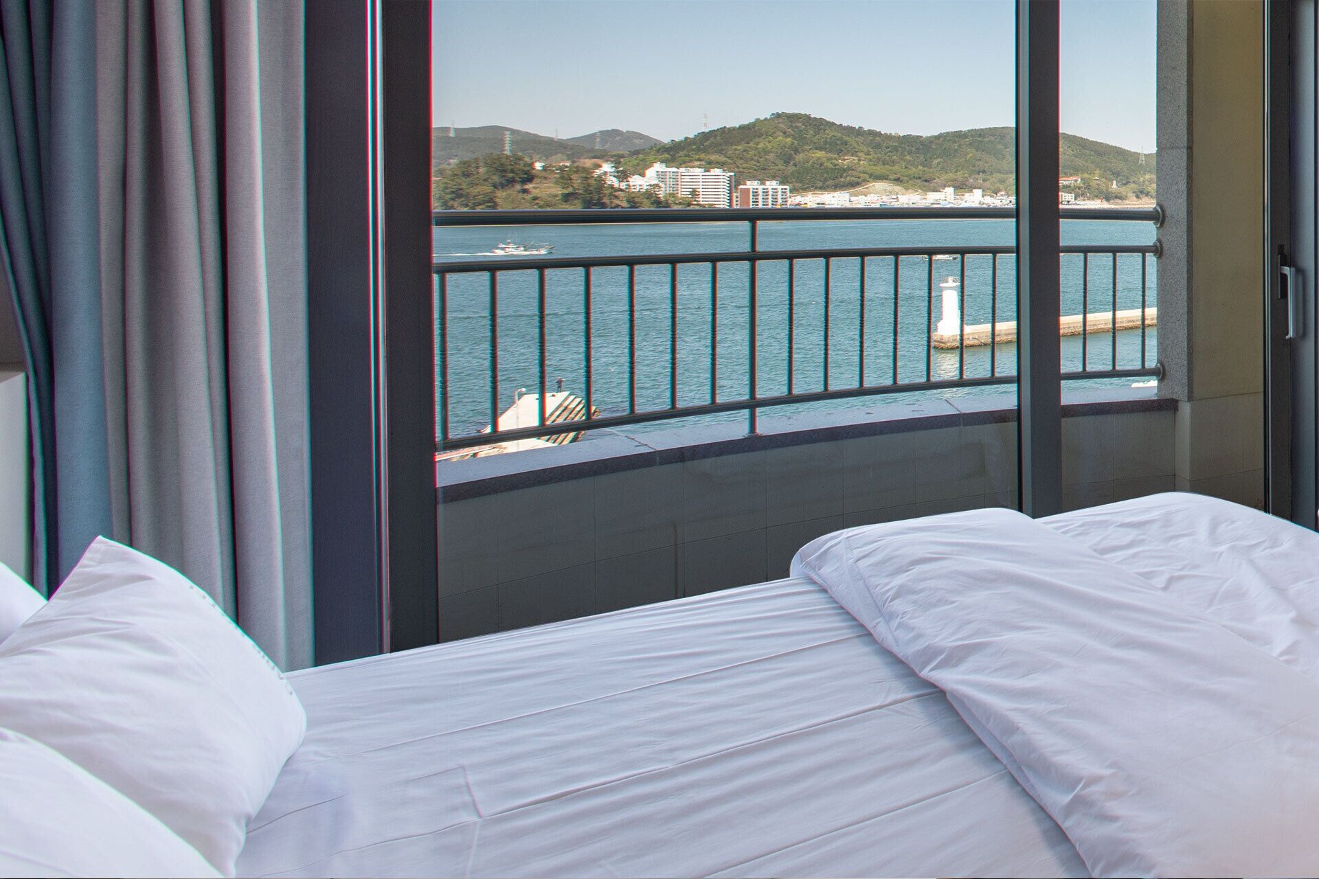 A hotel room with a bed, a view of a body of water, and a railing.