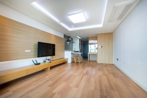 Un apartamento moderno con piso de madera, un televisor de pantalla plana montado en la pared, una zona de cocina y un comedor.