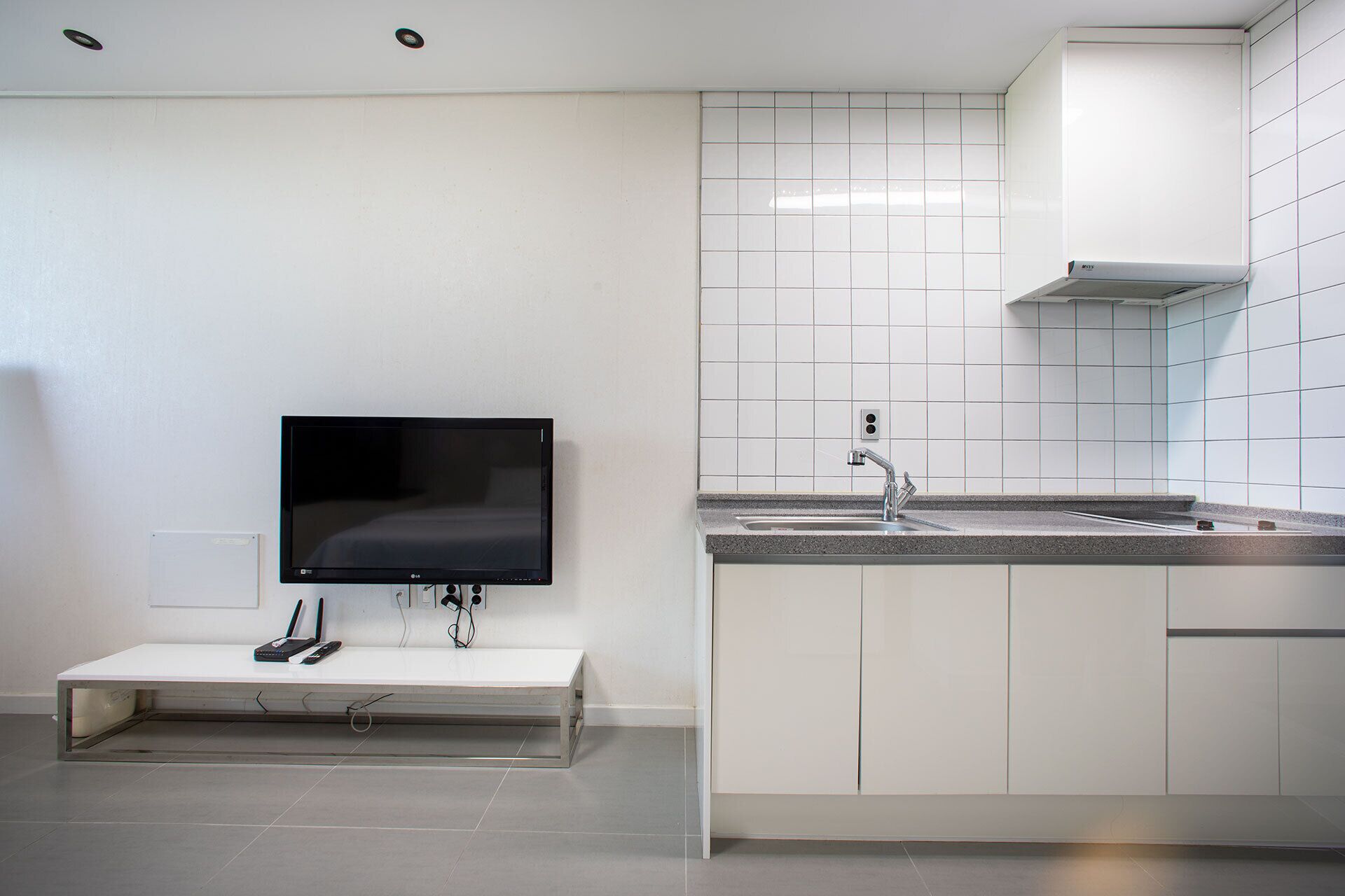 Una cocina moderna con armarios blancos, un televisor integrado y un lavamanos de acero inoxidable.