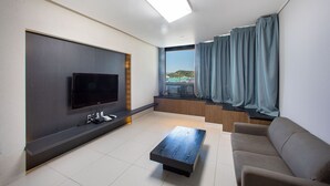 Una sala de estar moderna con una televisión de pantalla plana, una mesa de centro, un sofá y un amplio ventanal con cortinas.